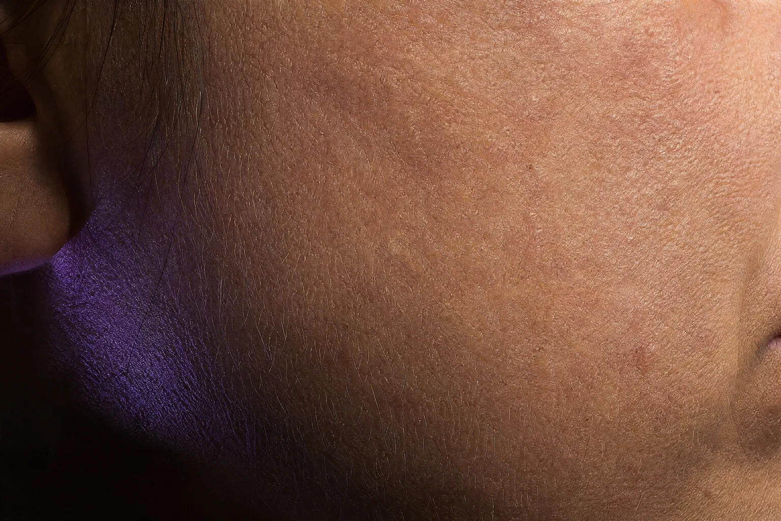 Extreme macro photograph of skin under raking light showing pores, fine vellus hair and natural texture
